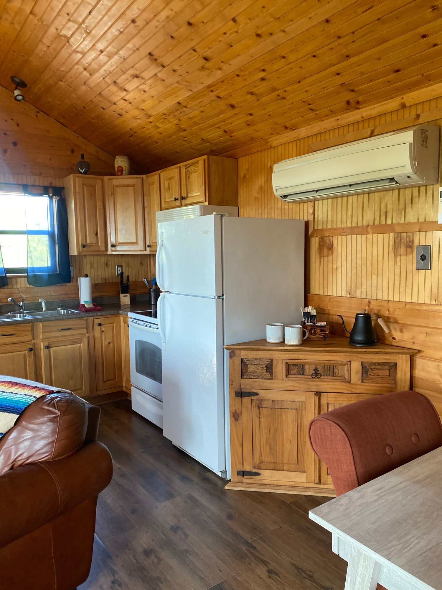 A kitchen in a log cabin with a refrigerator , stove , sink and chair.