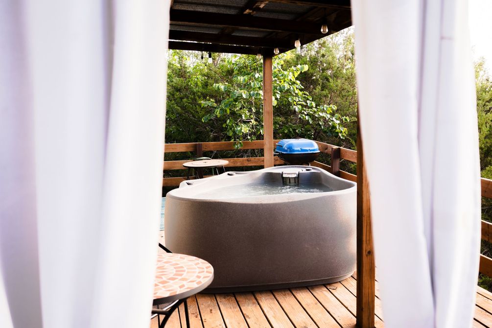 A hot tub is sitting on a wooden deck under a canopy.