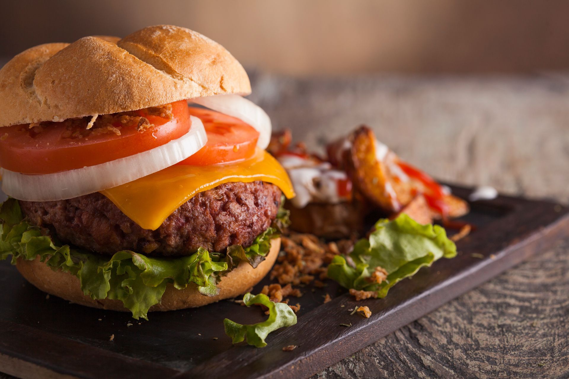 A hamburger with cheese , lettuce , tomato and onions on a bun on a cutting board.