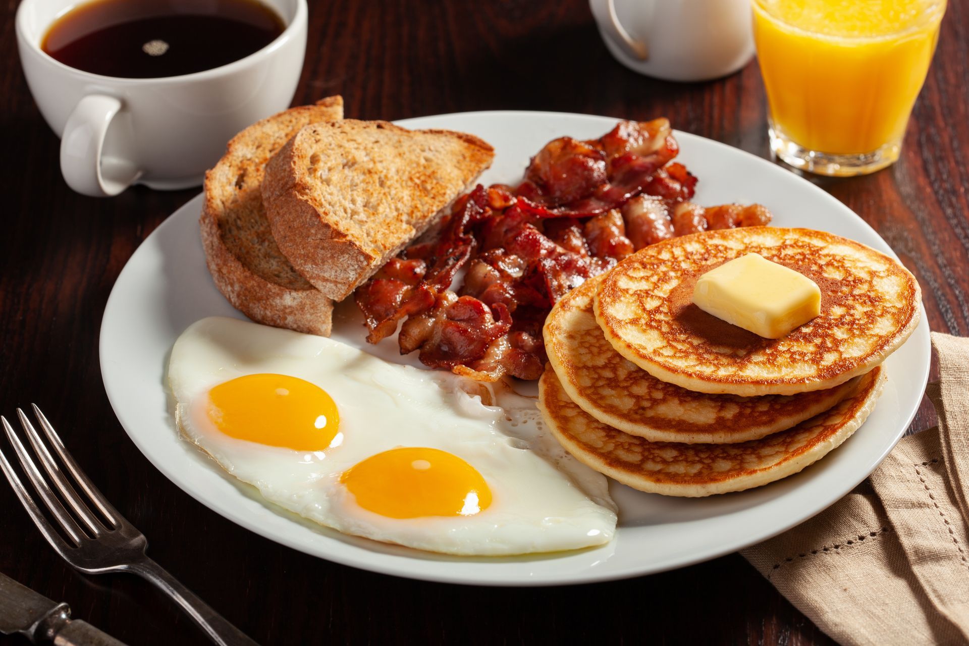 A white plate topped with eggs , pancakes , bacon and toast.