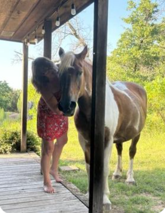 A little girl is hugging a horse on a porch.