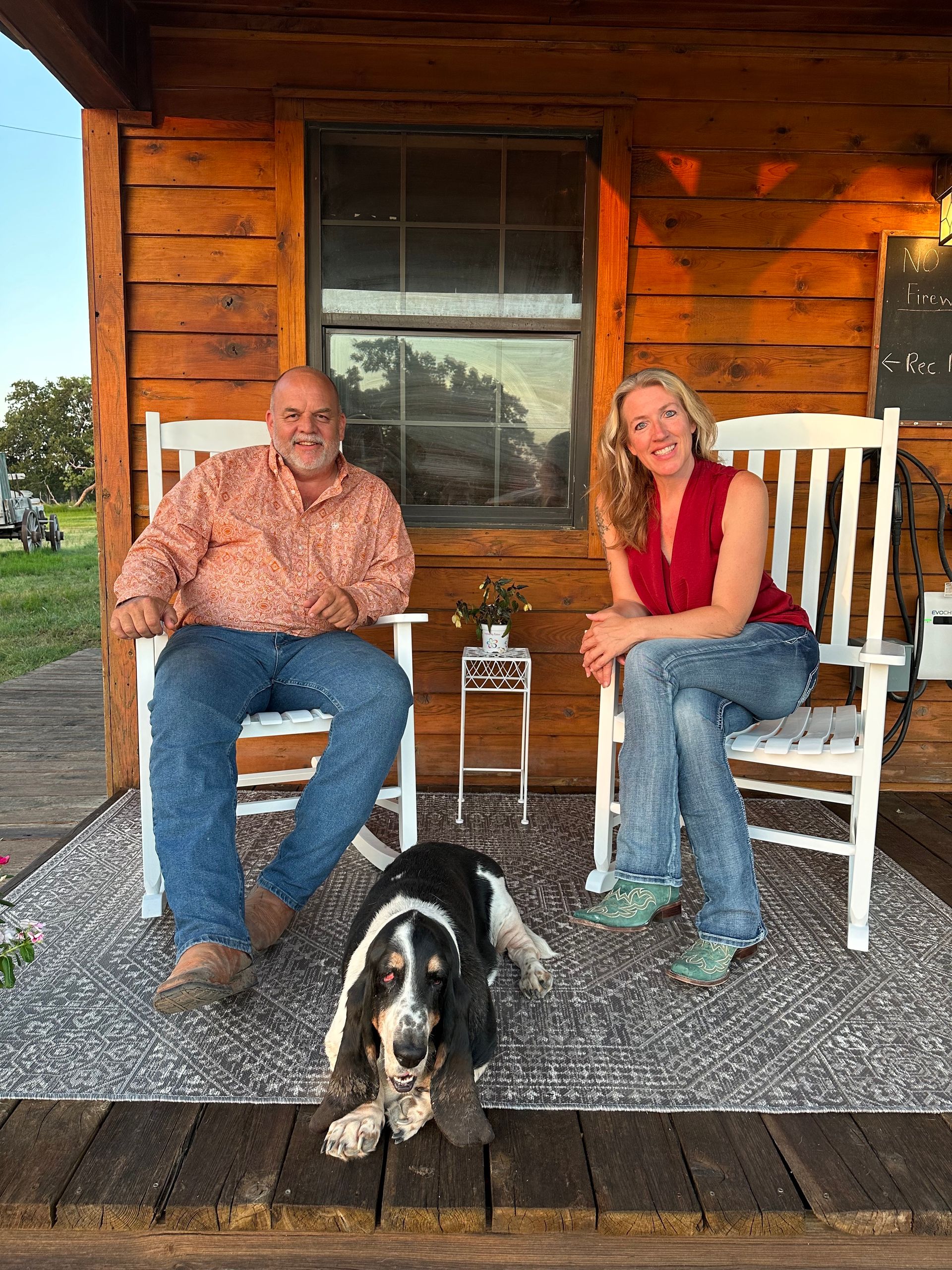 A man and a woman are sitting in rocking chairs on a porch with a dog.