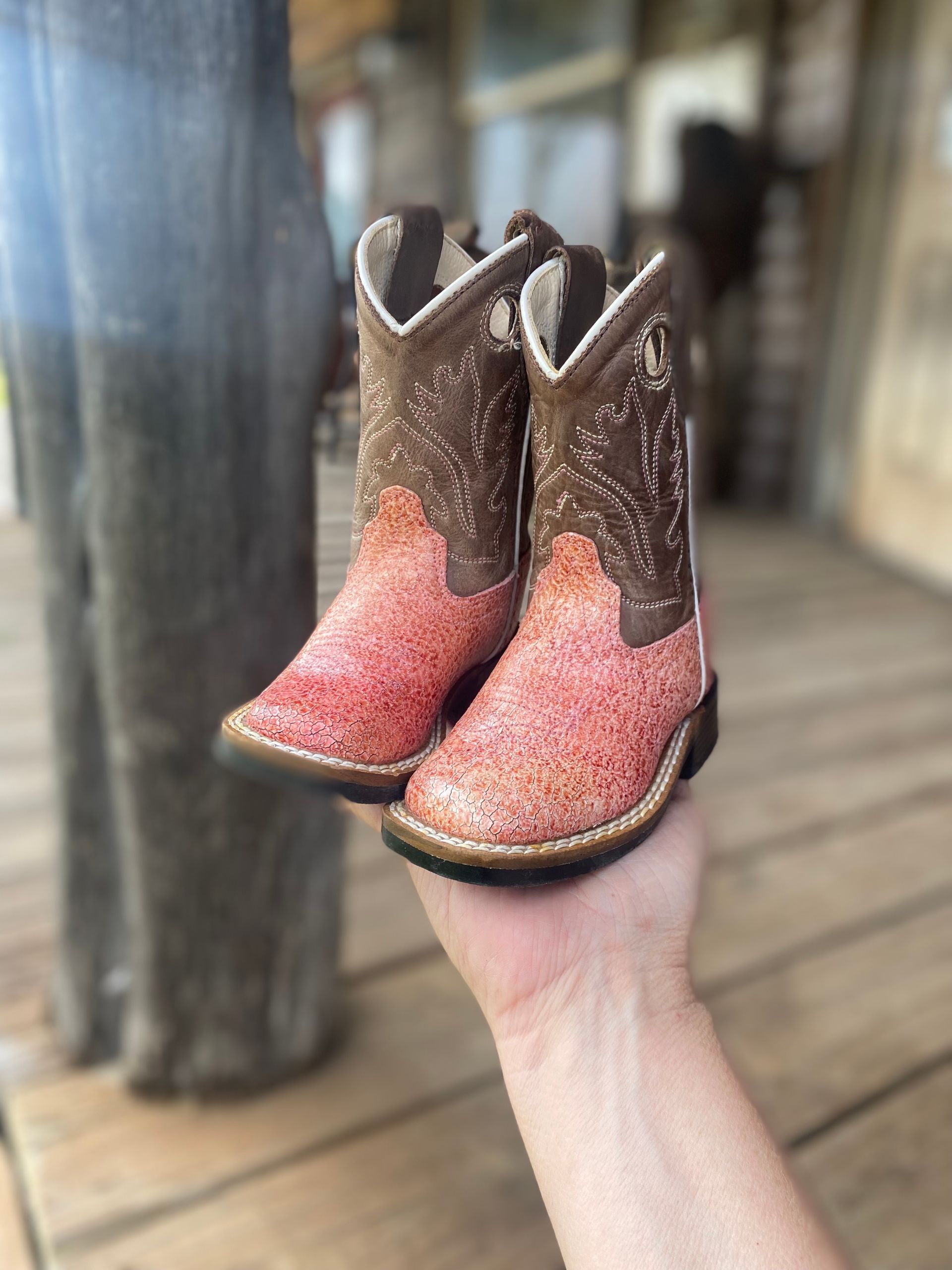 A person is holding a pair of pink and brown cowboy boots in their hand.