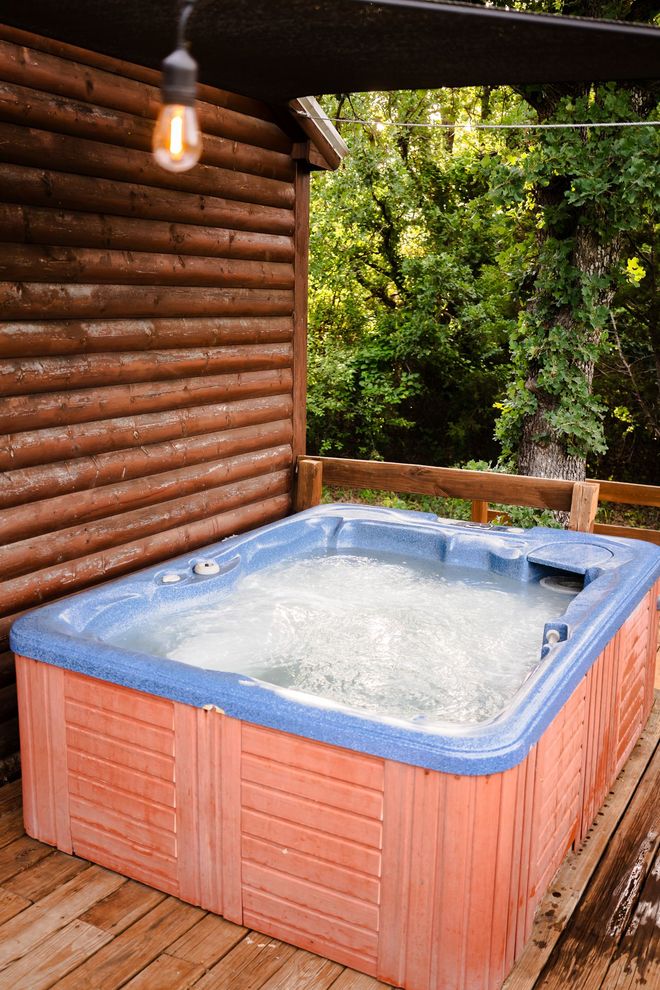 A hot tub is sitting on a wooden deck next to a log cabin.