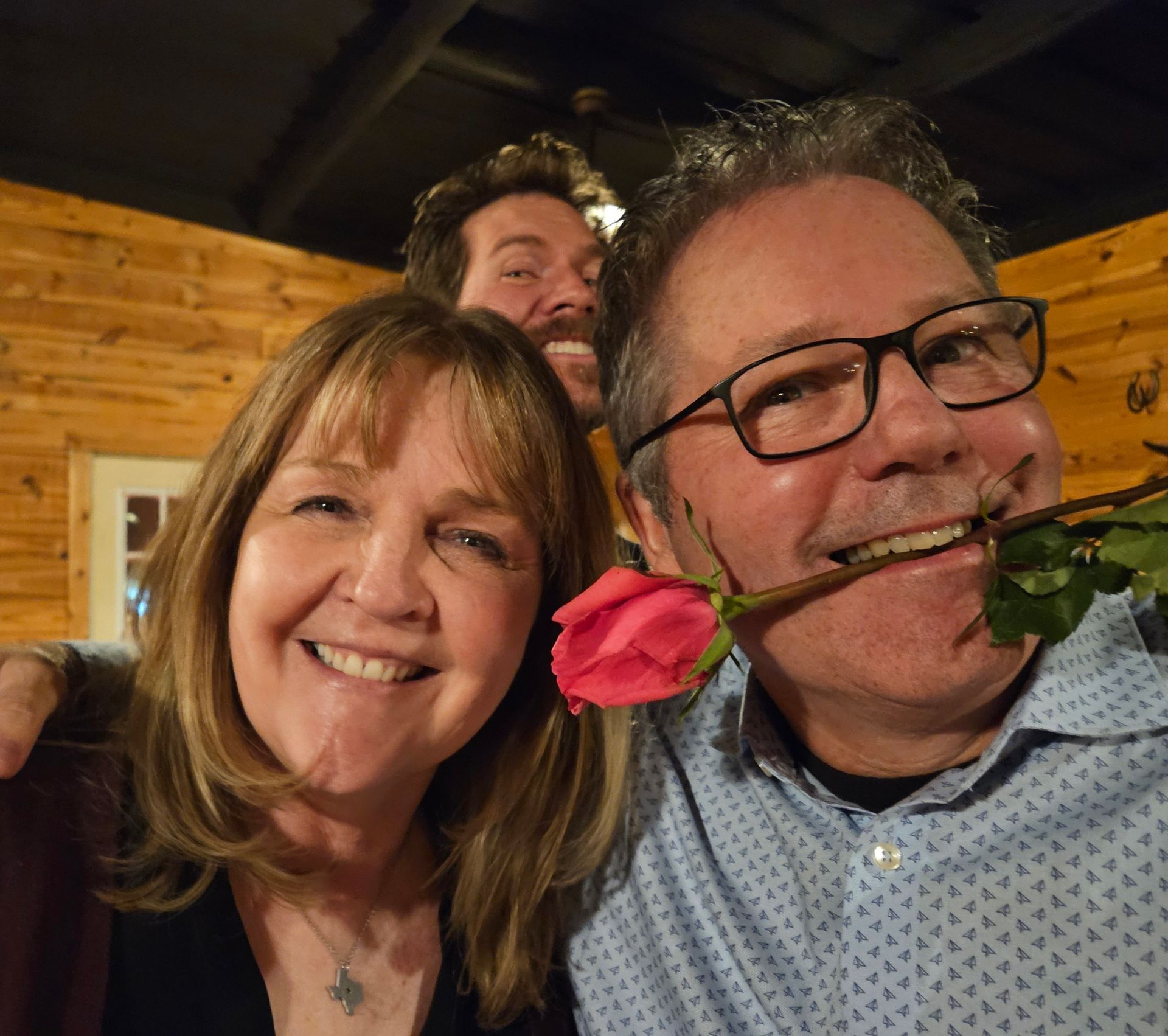 A man with glasses is holding a pink rose in his mouth