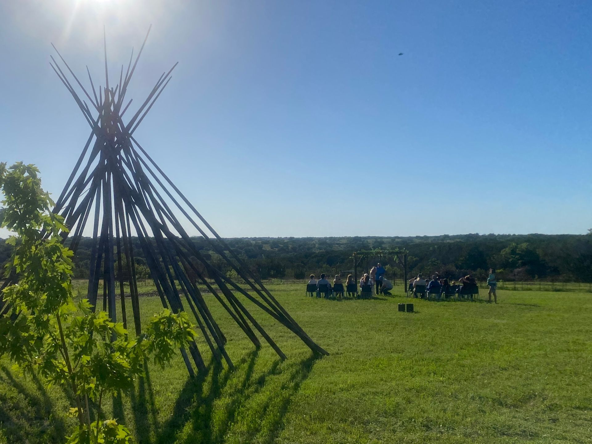 A group of people are sitting around a teepee in a grassy field.