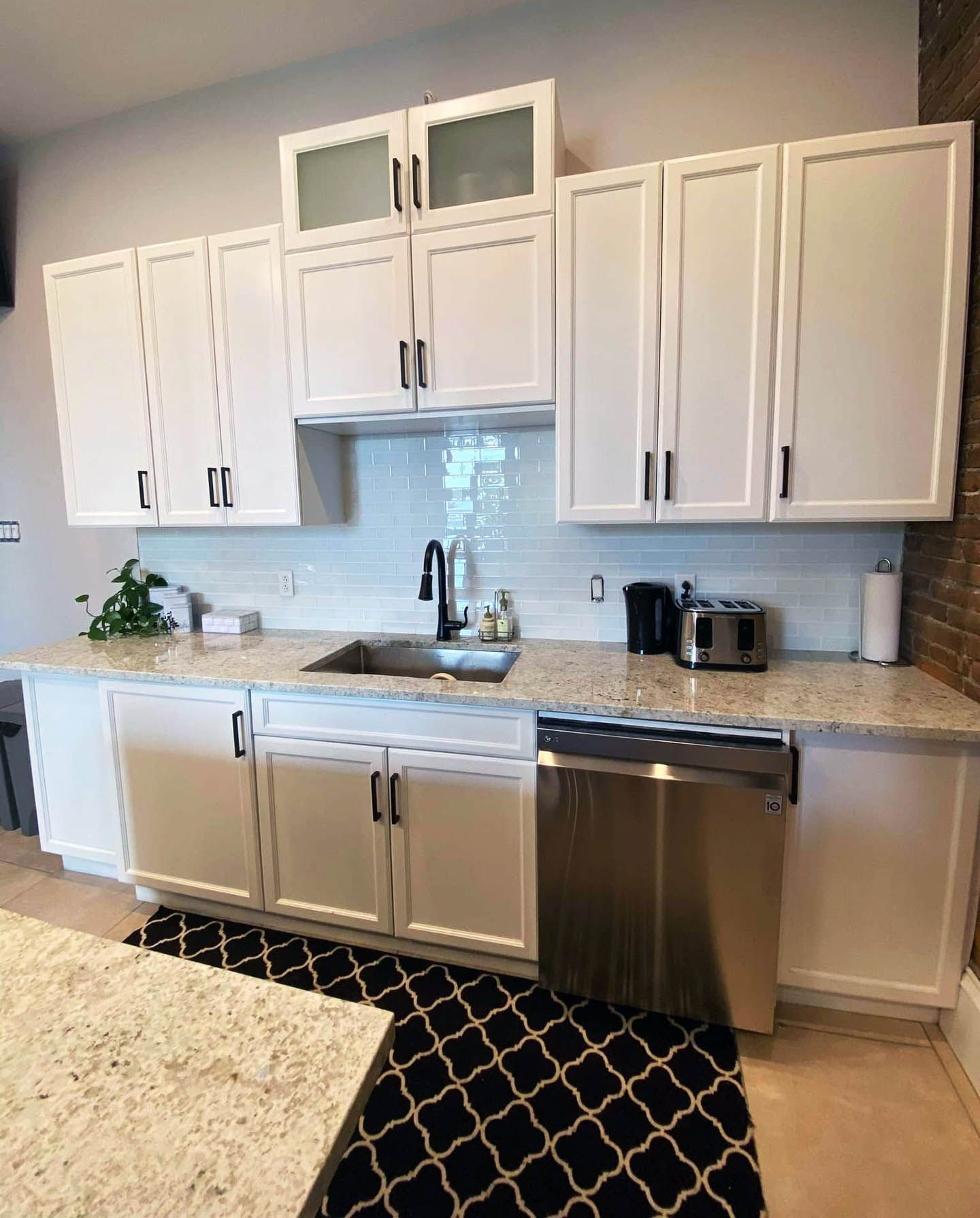 Une cuisine avec des armoires blanches, des comptoirs en granit, des appareils en acier inoxydable et un tapis noir et blanc.