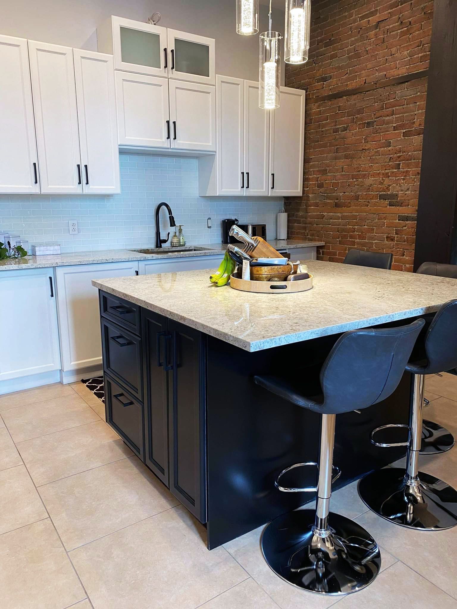 Une cuisine avec des armoires blanches, un grand îlot et un mur de briques.