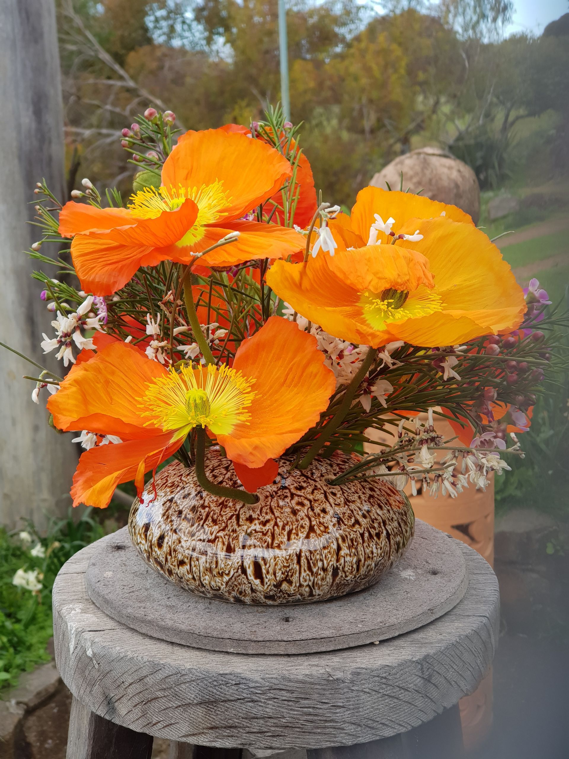 A PoseyPot filled with orange flowers is sitting on a stone stool.