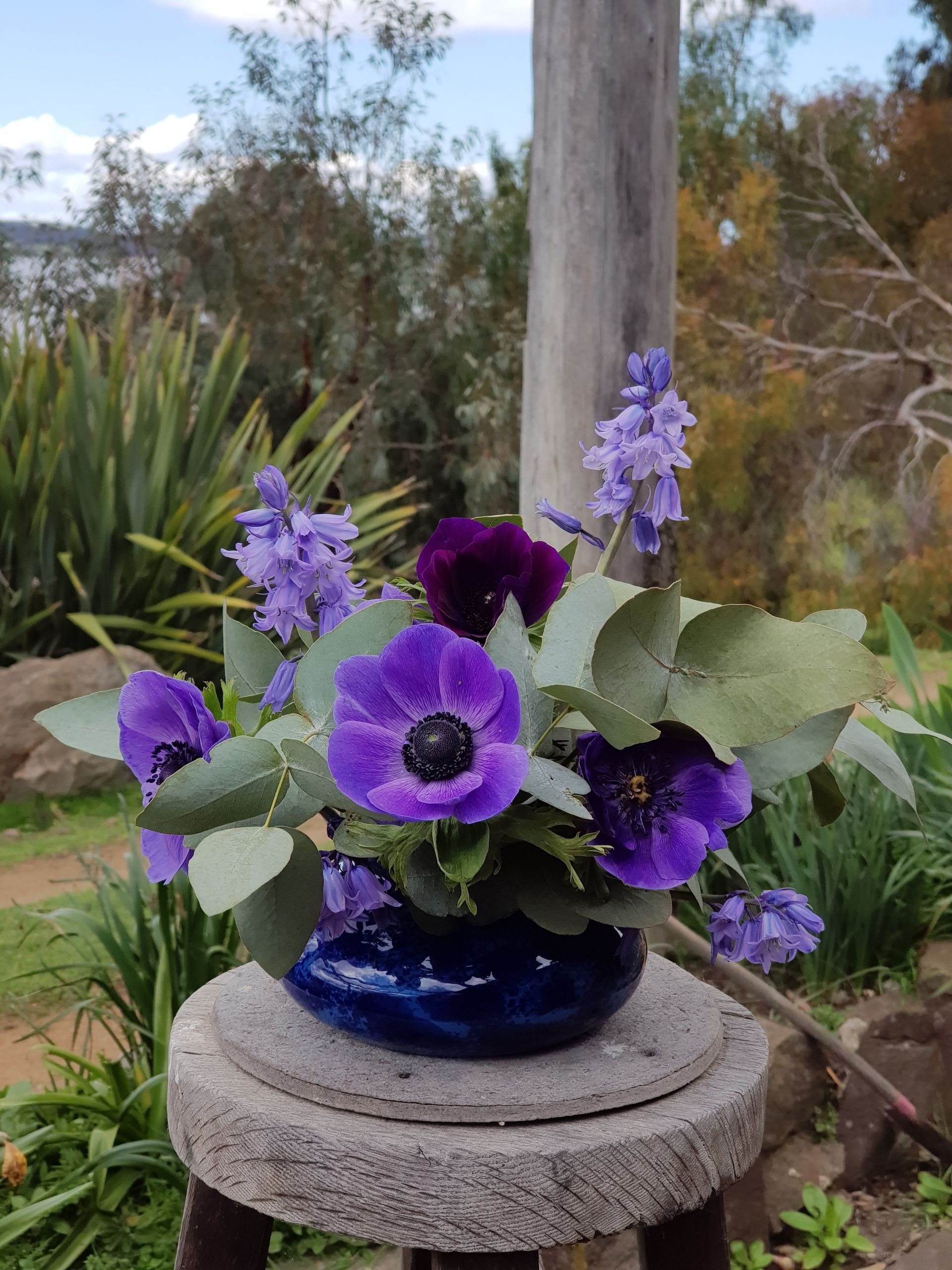 A PoseyPot filled with purple flowers is sitting on a stone stool.