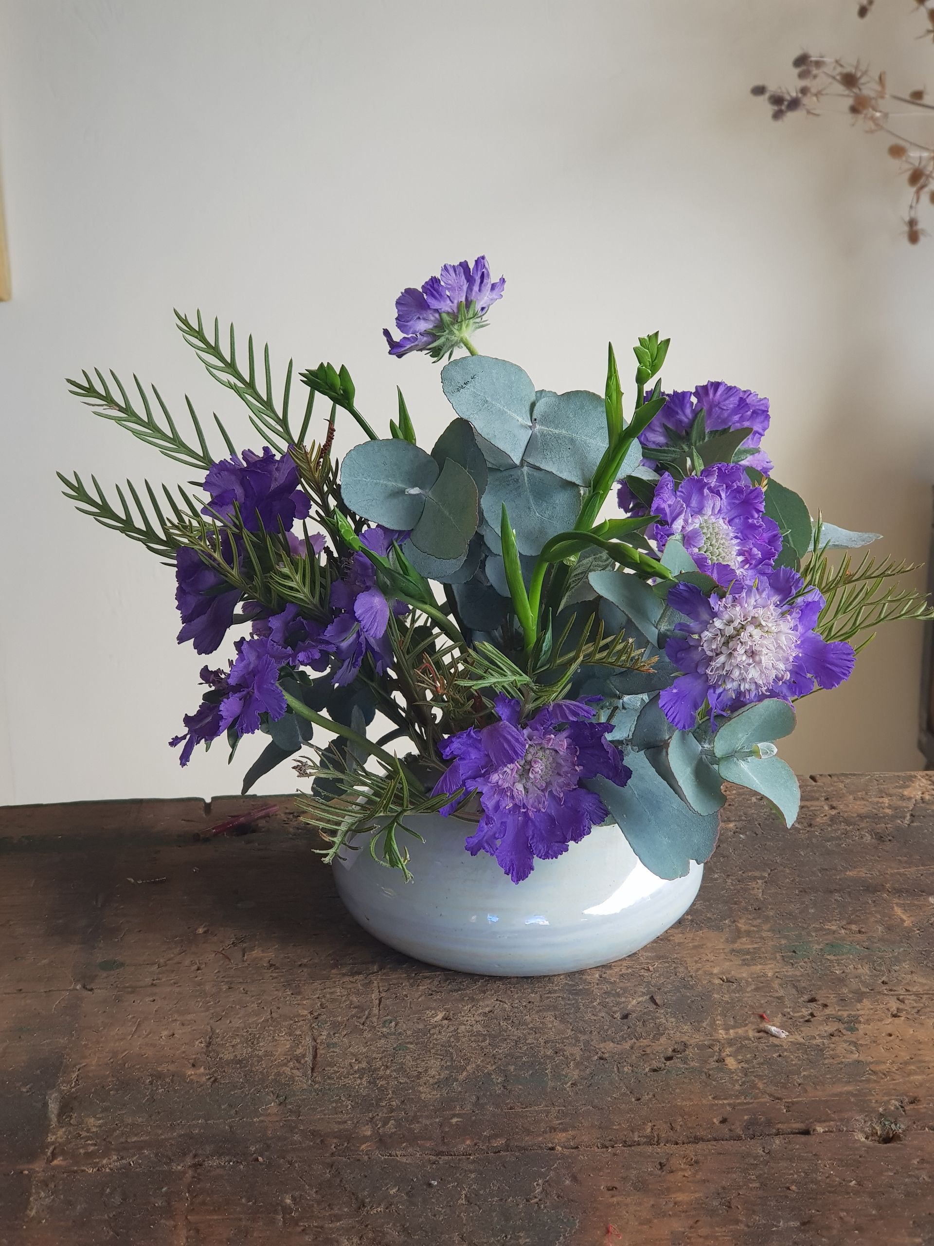 A PoseyPot filled with purple flowers is sitting on a wooden table.