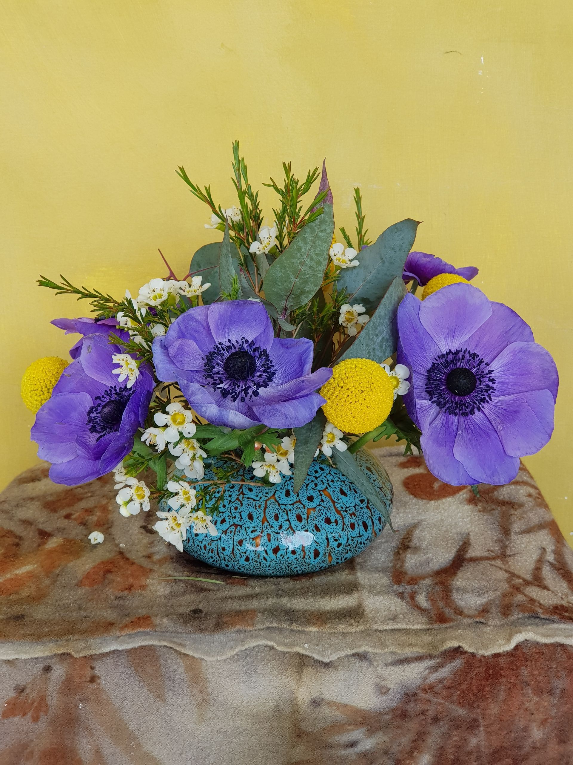 Purple and yellow flowers in a blue PoseyPot on a table