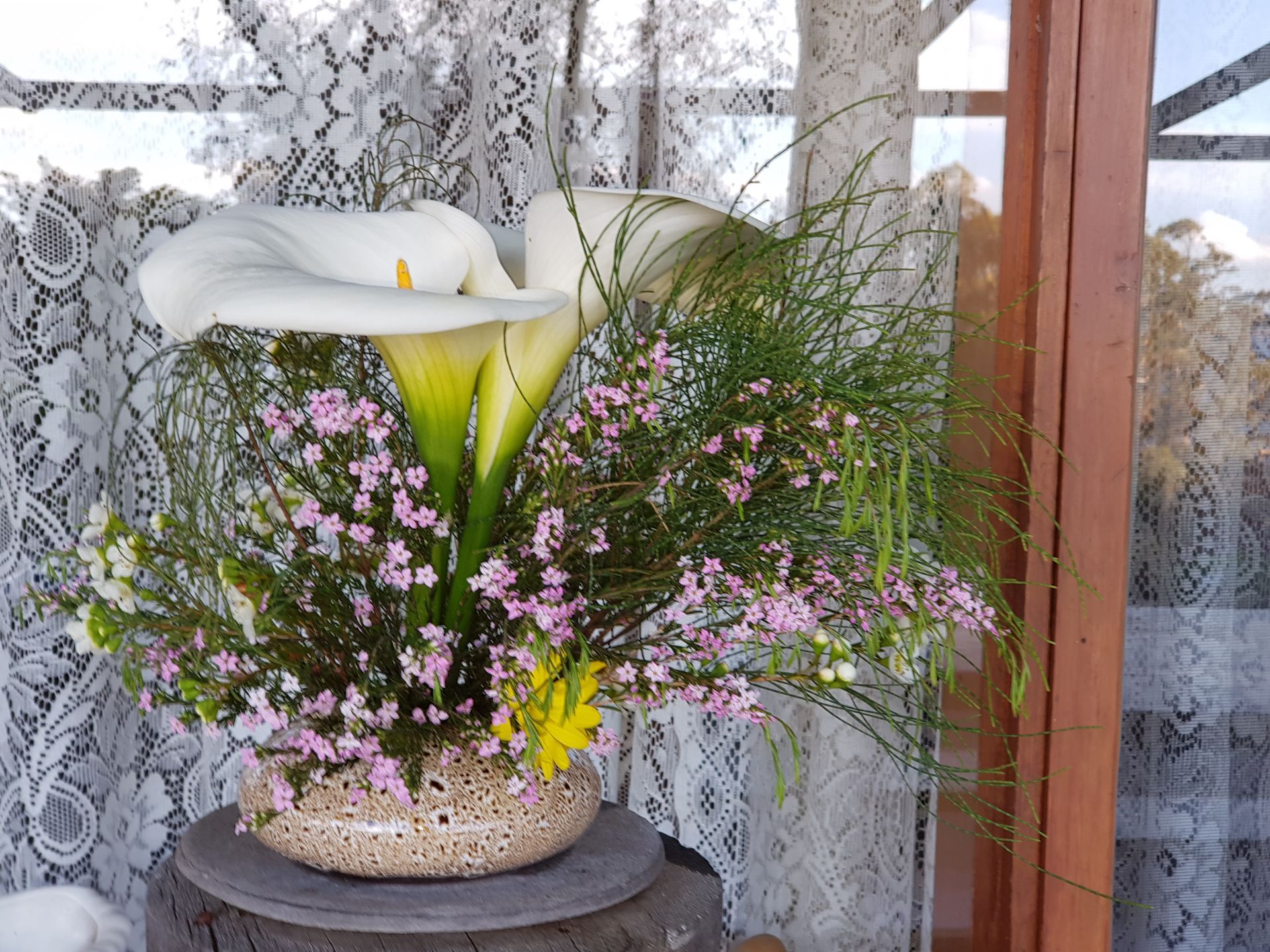 A PoseyPot filled with flowers is sitting on a table in front of a window.