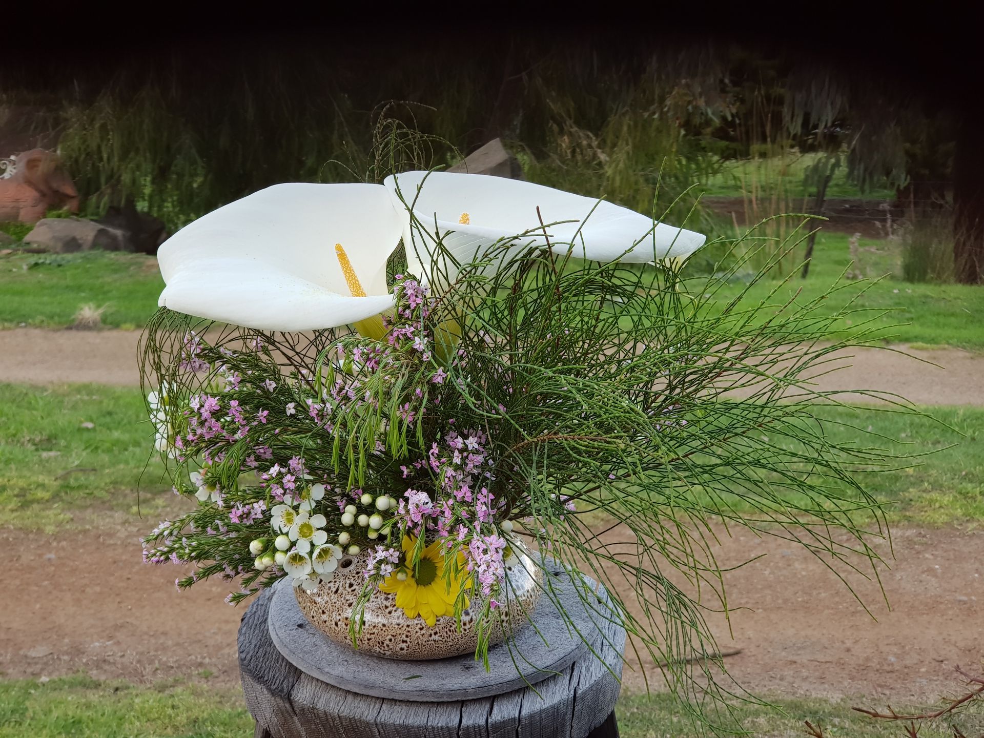 A PoseyPot of flowers is sitting on top of a wooden stump.
