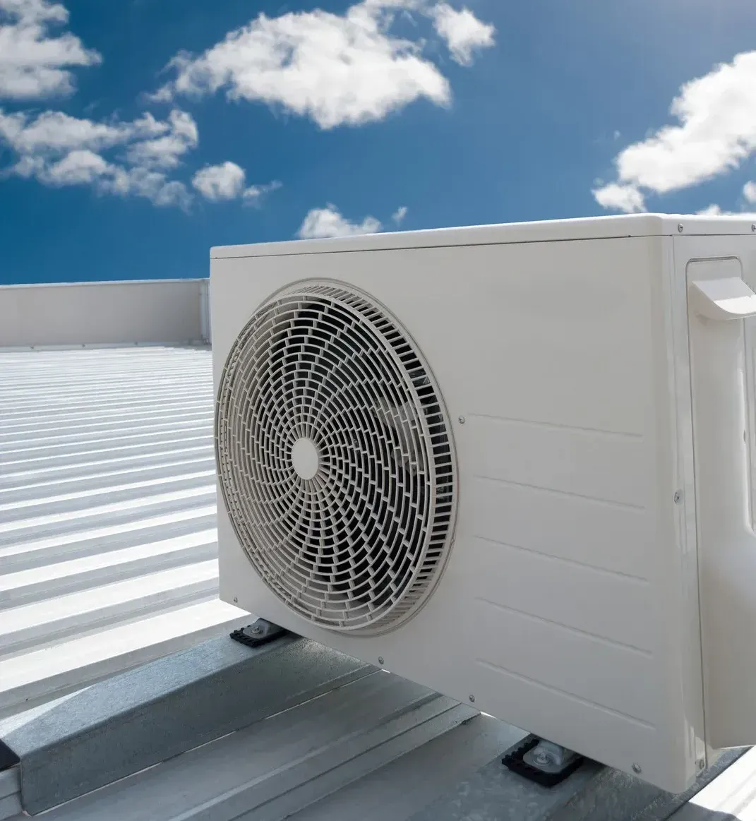 White air conditioning unit on a white metal roof against a blue sky with clouds.