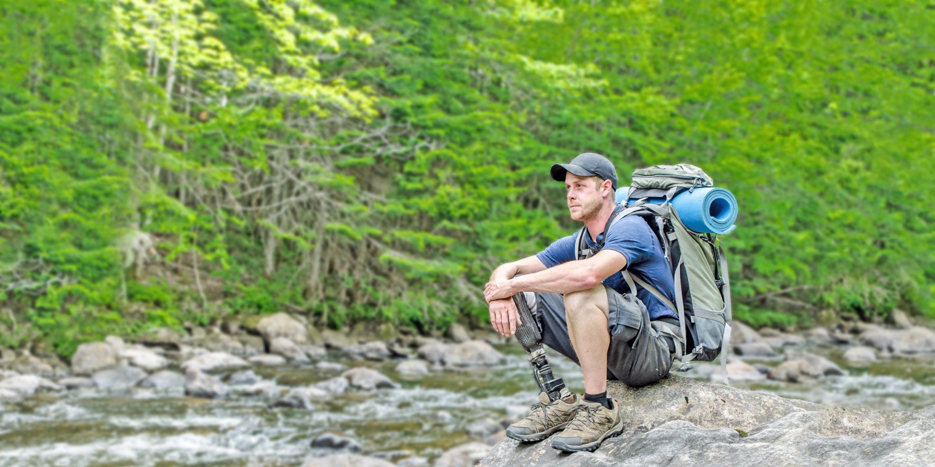 A man with a backpack is sitting on a rock near a river.