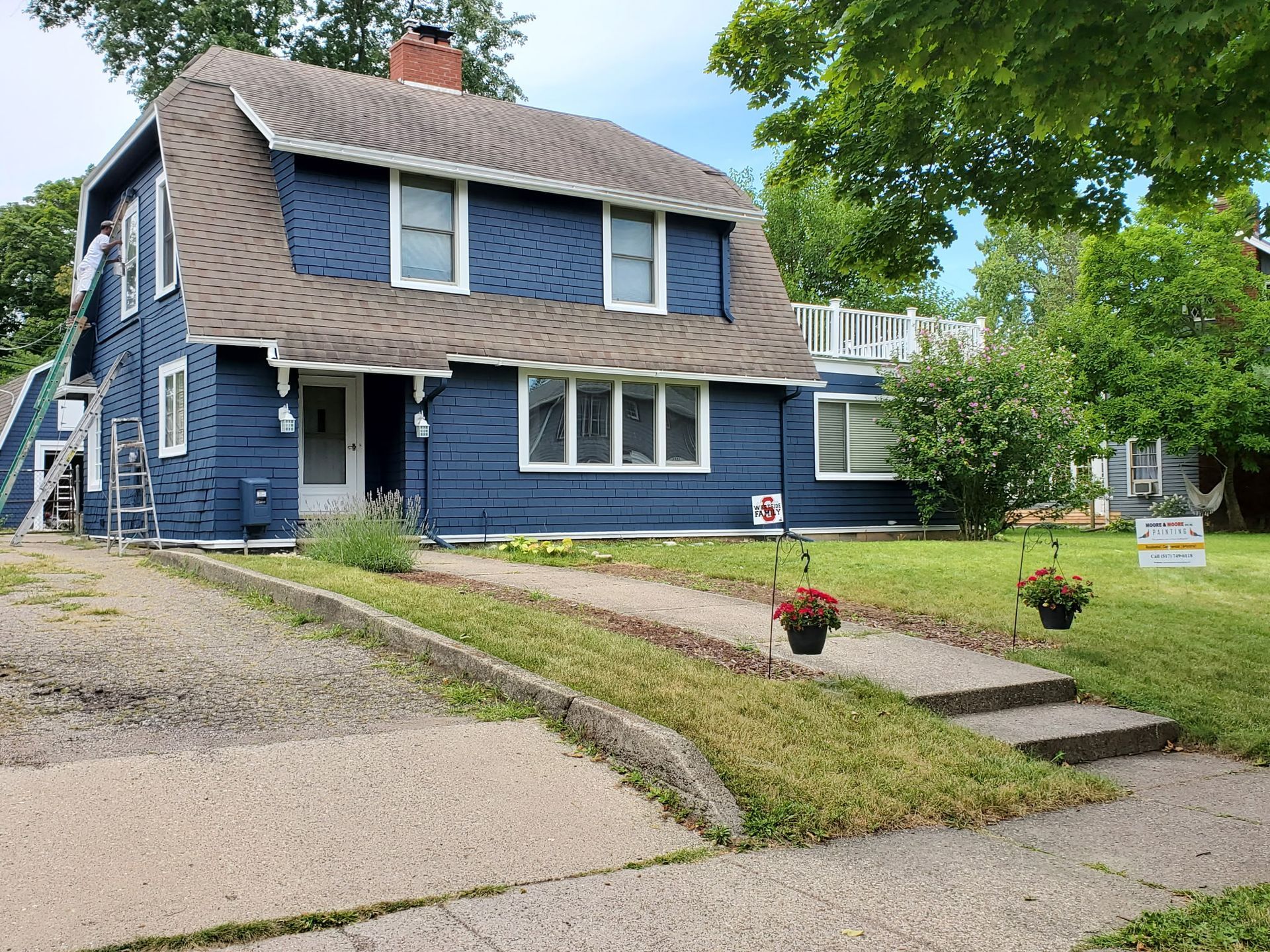 Blue two-story house with a gambrel roof and a small front yard; a concrete path leads to the front door.