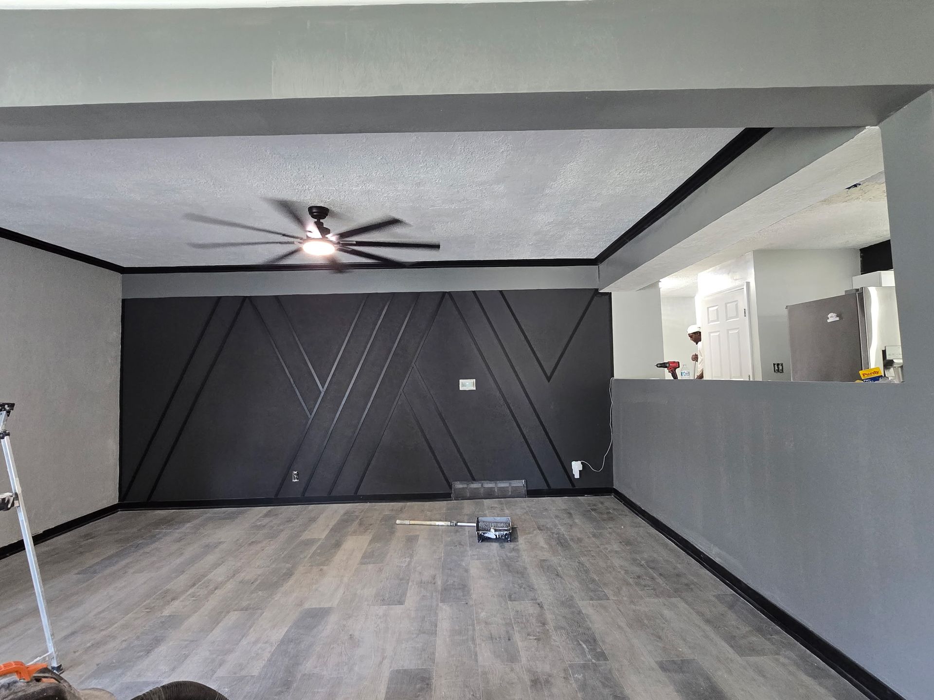 Living room with gray walls, wood flooring, black accent wall, and ceiling fan.