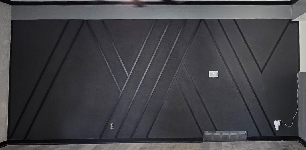 Black geometric accent wall with wooden trim. Electrical outlets and vent visible.
