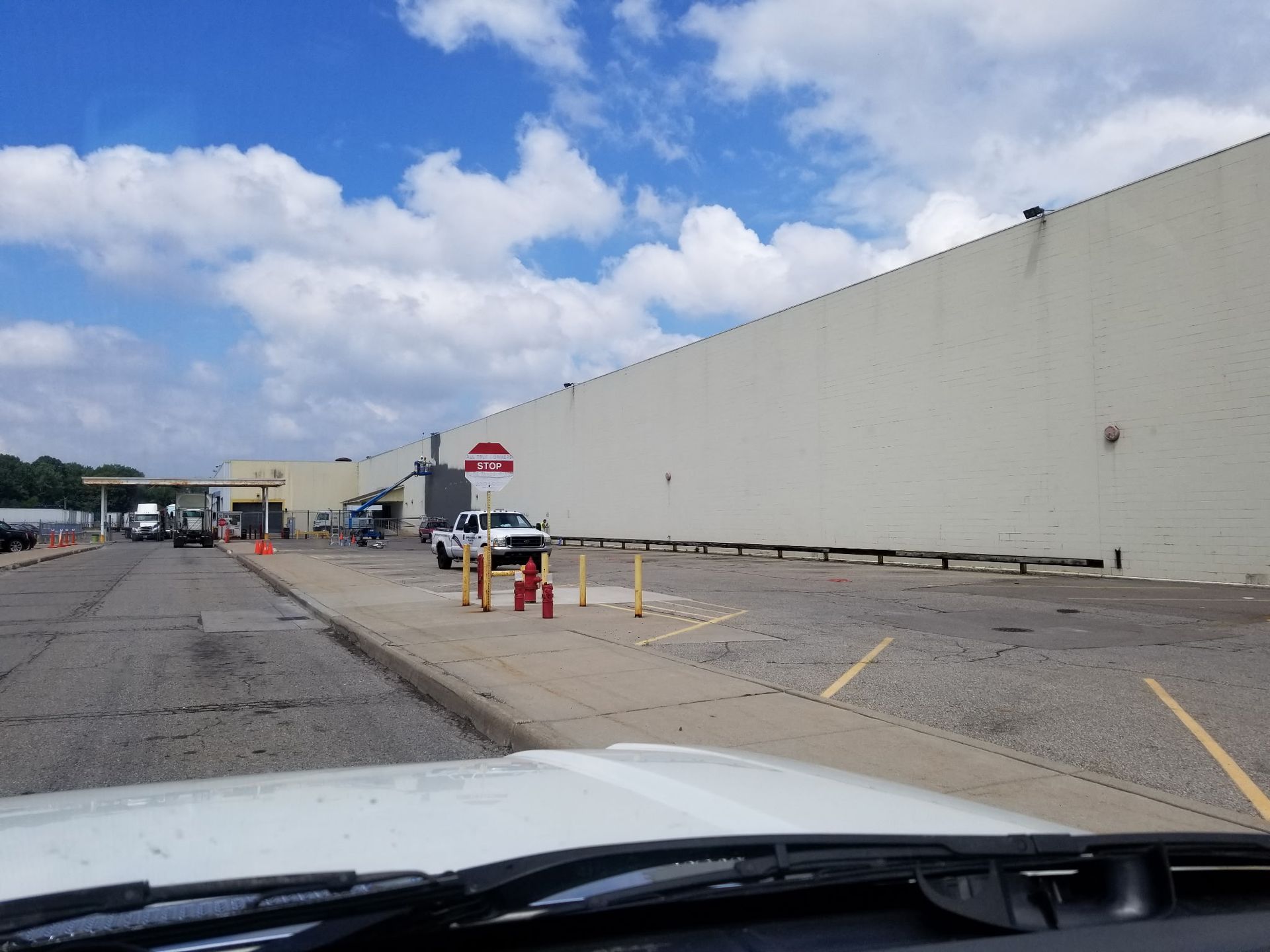 Exterior of a large beige building with vehicles and traffic cones on a concrete surface under a partly cloudy sky.