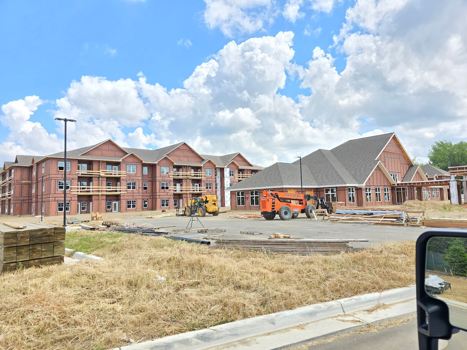 Workers in a lift painting a large building exterior gray. Blue lift, gray paint, cloudy sky.