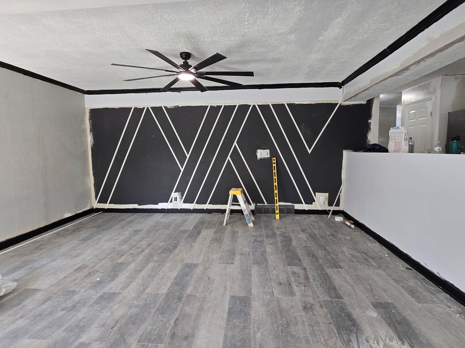 Living room with black accent wall, white geometric lines, gray flooring, and black trim.
