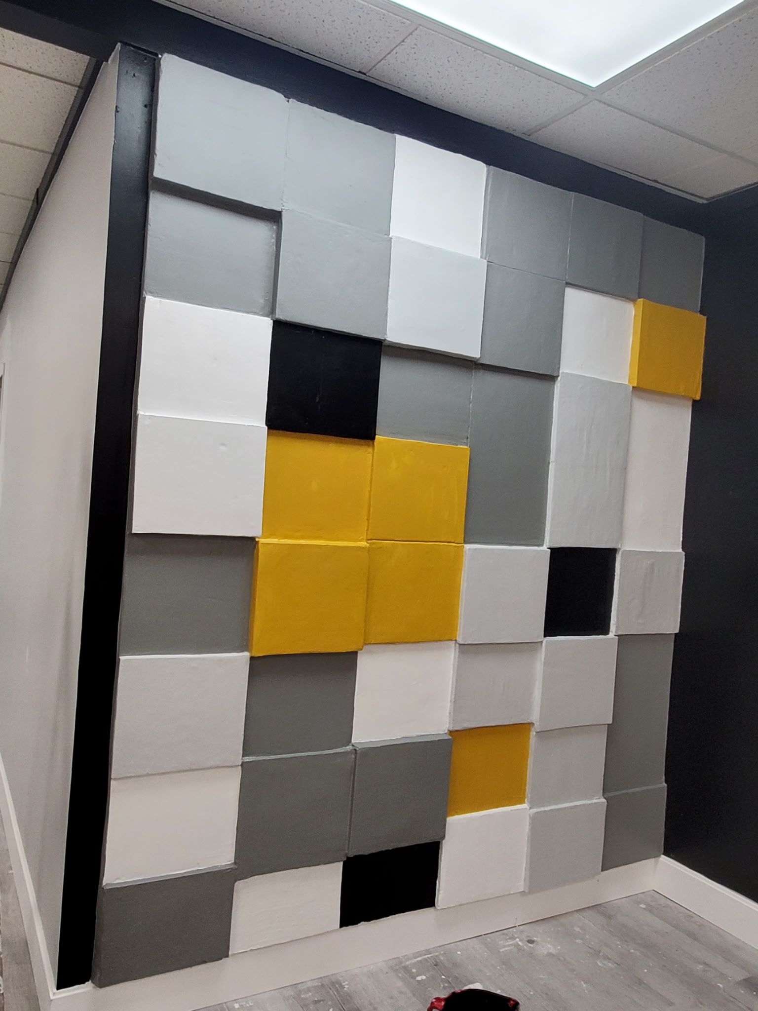 A wall with square, color-blocked acoustic panels in white, gray, yellow, and black.