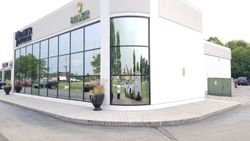 Building with large glass windows reflecting trees and sky, corner view.