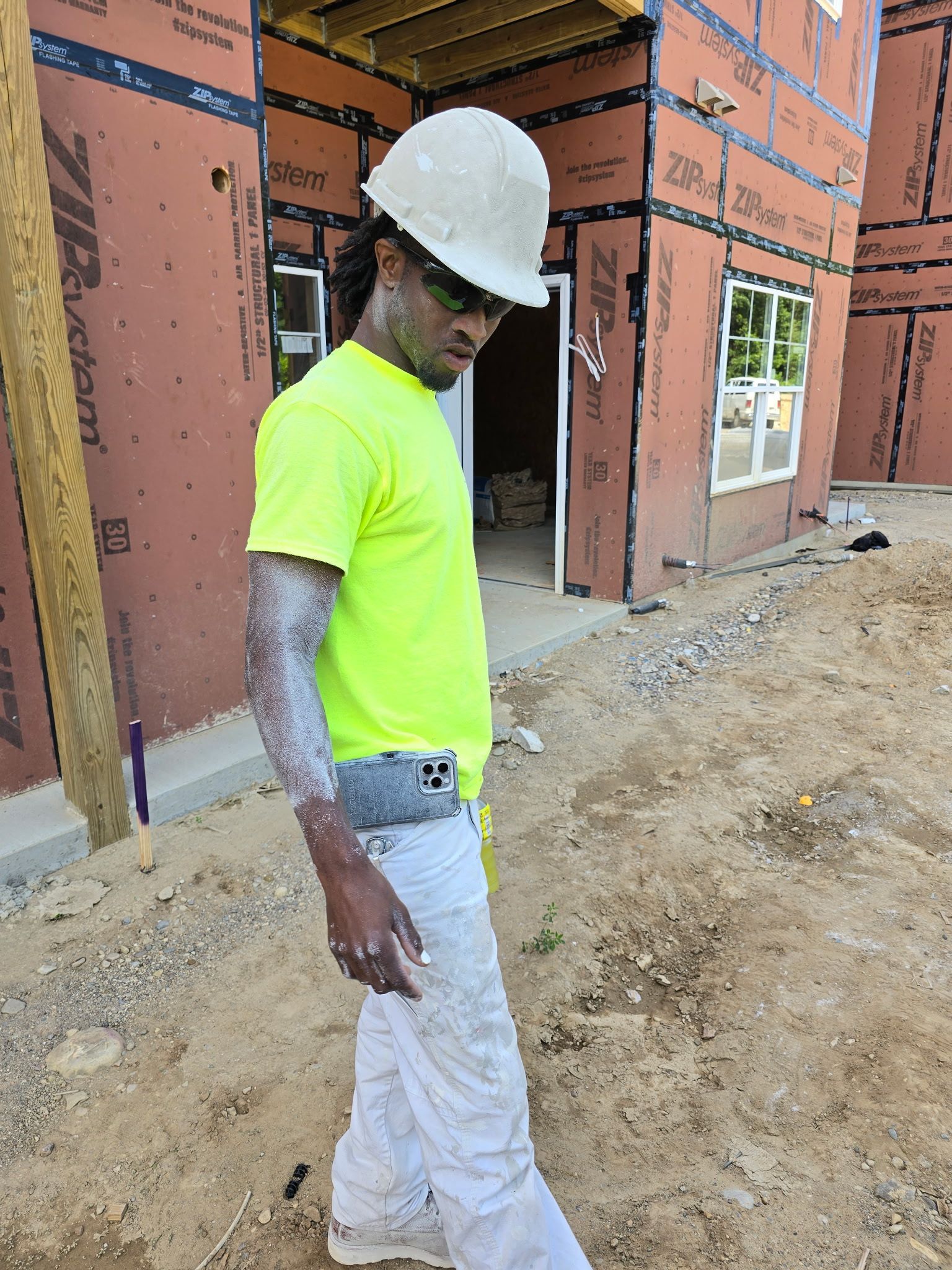 Construction worker in a hard hat and neon shirt, covered in dust, standing at a construction site.