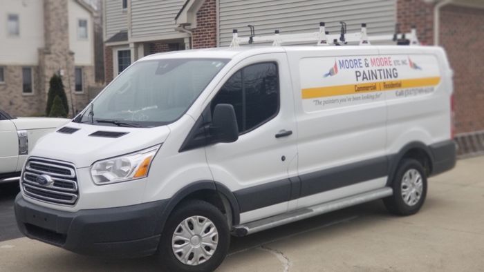 White Ford Transit van with Moore & Moore Painting logo parked in front of a building.