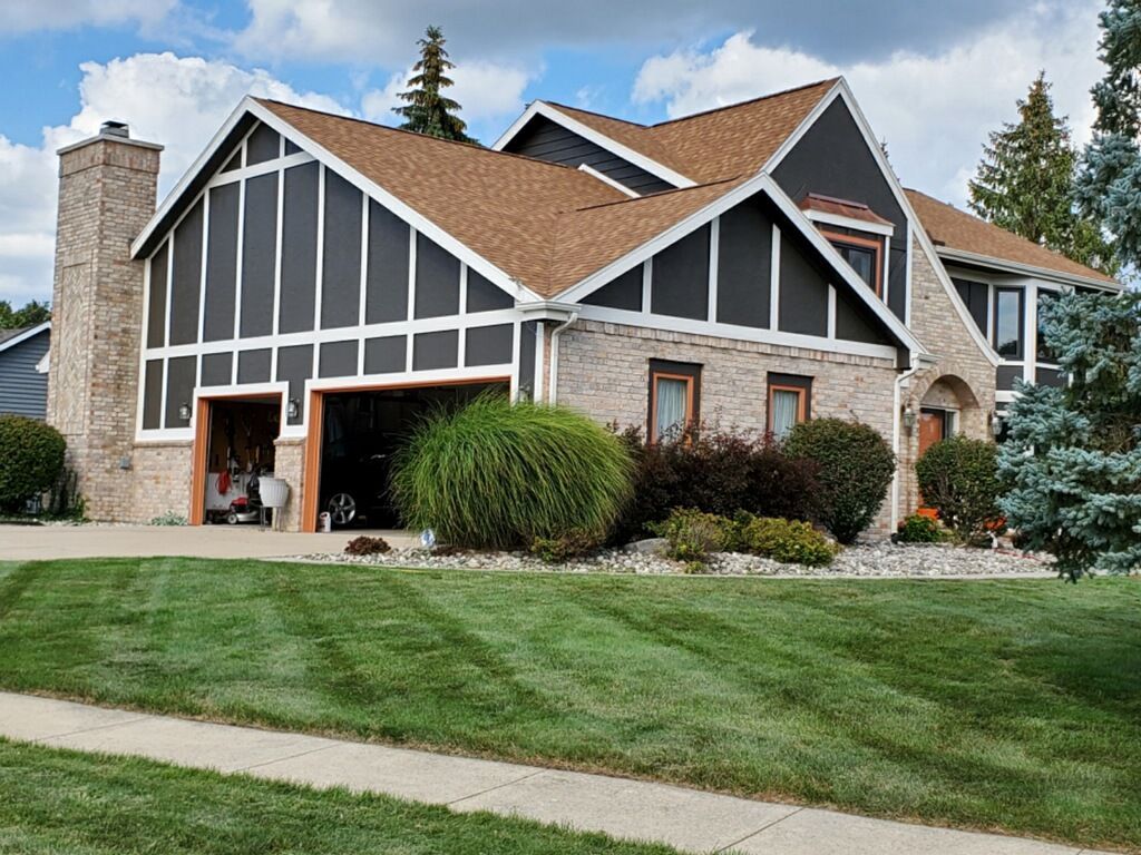 House with brown roof, black trim, brick facade, and green lawn.
