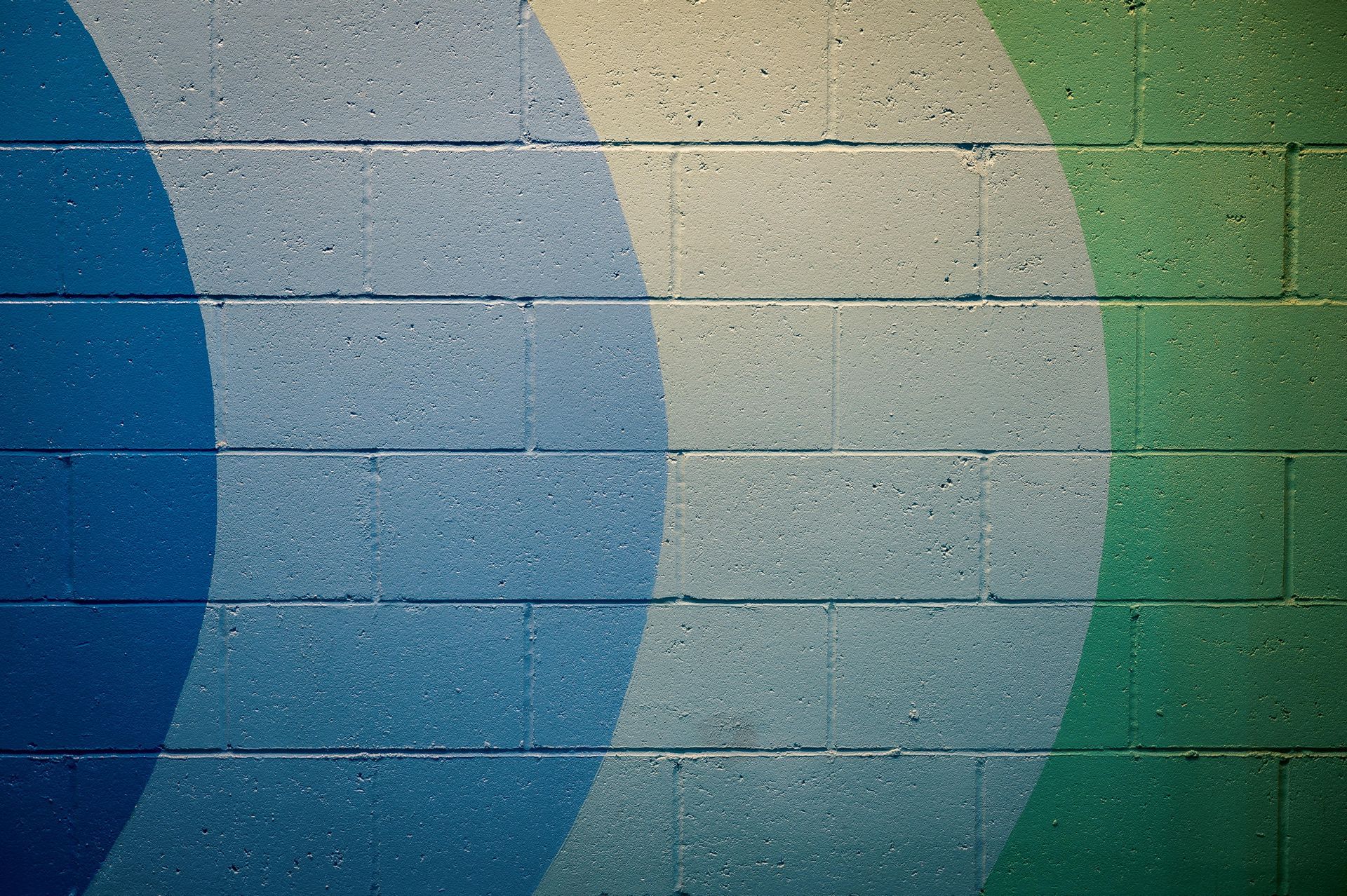 Blue, beige, and green curved stripes on a textured brick wall.