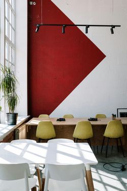 Modern office space with a red and white geometric wall, yellow chairs, and wooden table.