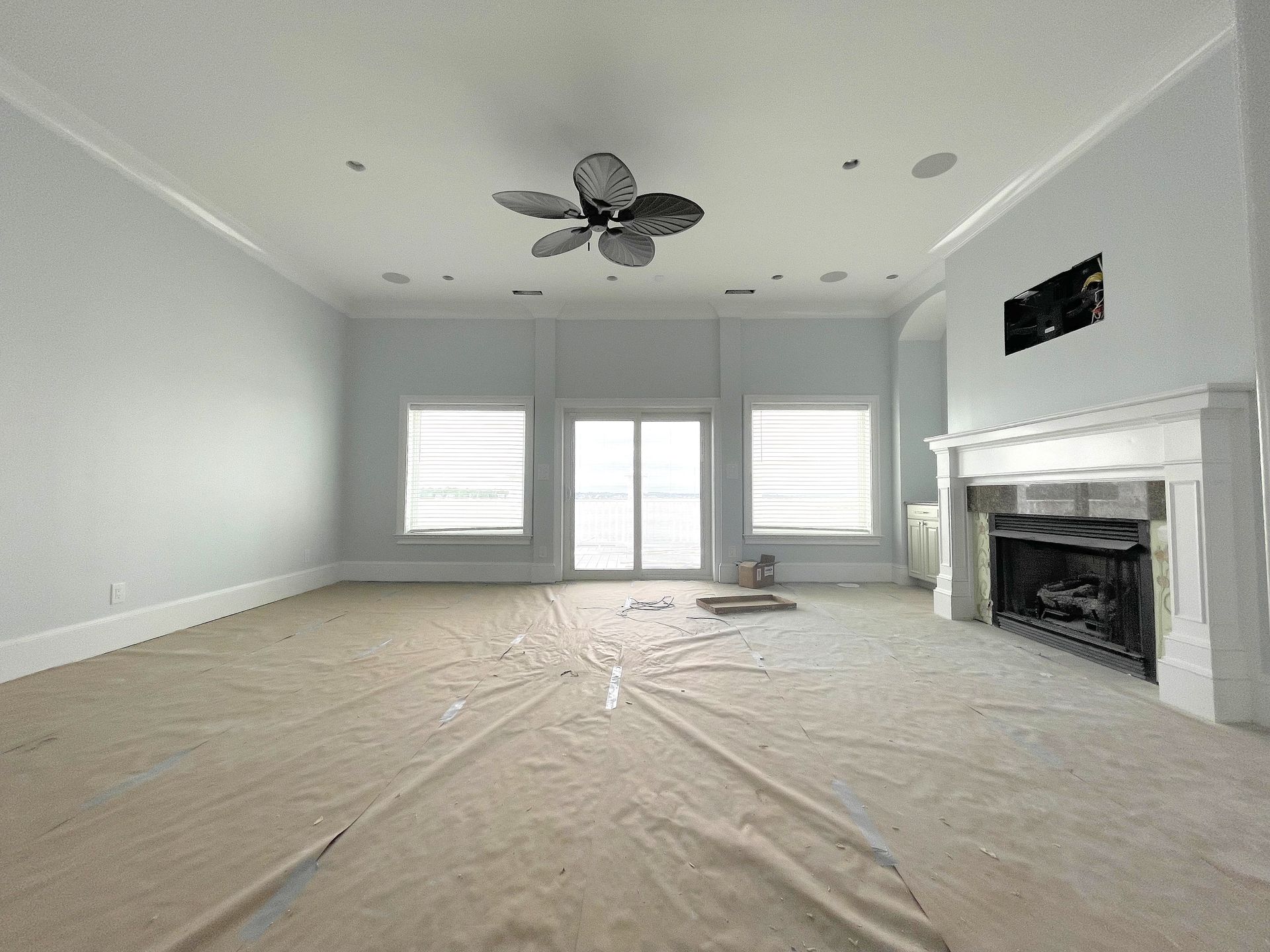 Empty living room with light blue walls, white trim, and a fireplace. Floor covered with protective covering.