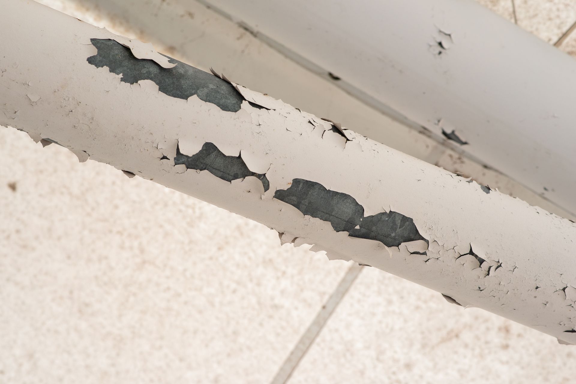 White pipes with peeling paint against a light-colored tile background.