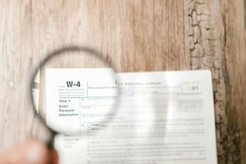 A person is holding a magnifying glass over a tax form.