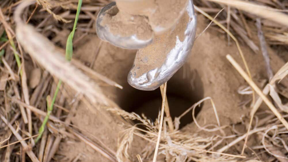 A Person is Digging a Hole in the Ground With a Drill — RCJJ Mini Loaders In Cairns, QLD