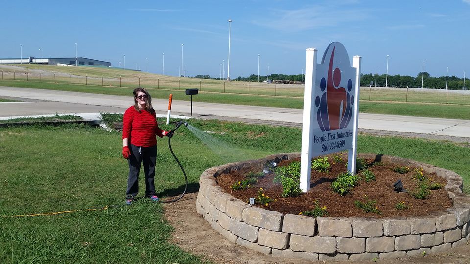 A woman in a red sweater is standing next to a sign in a garden.