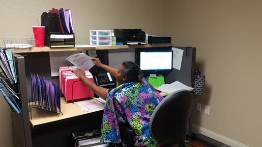 A woman is sitting at a desk in an office cubicle.