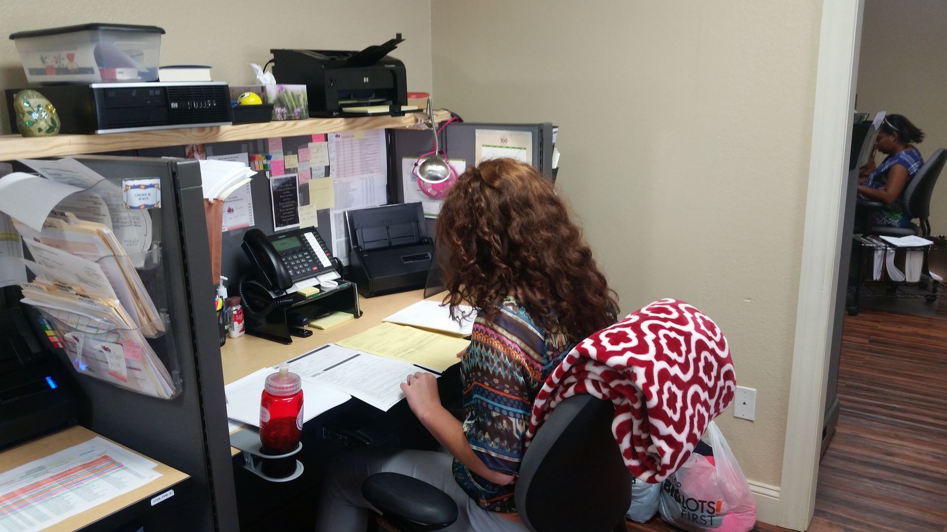 A woman is sitting at a desk in an office cubicle.