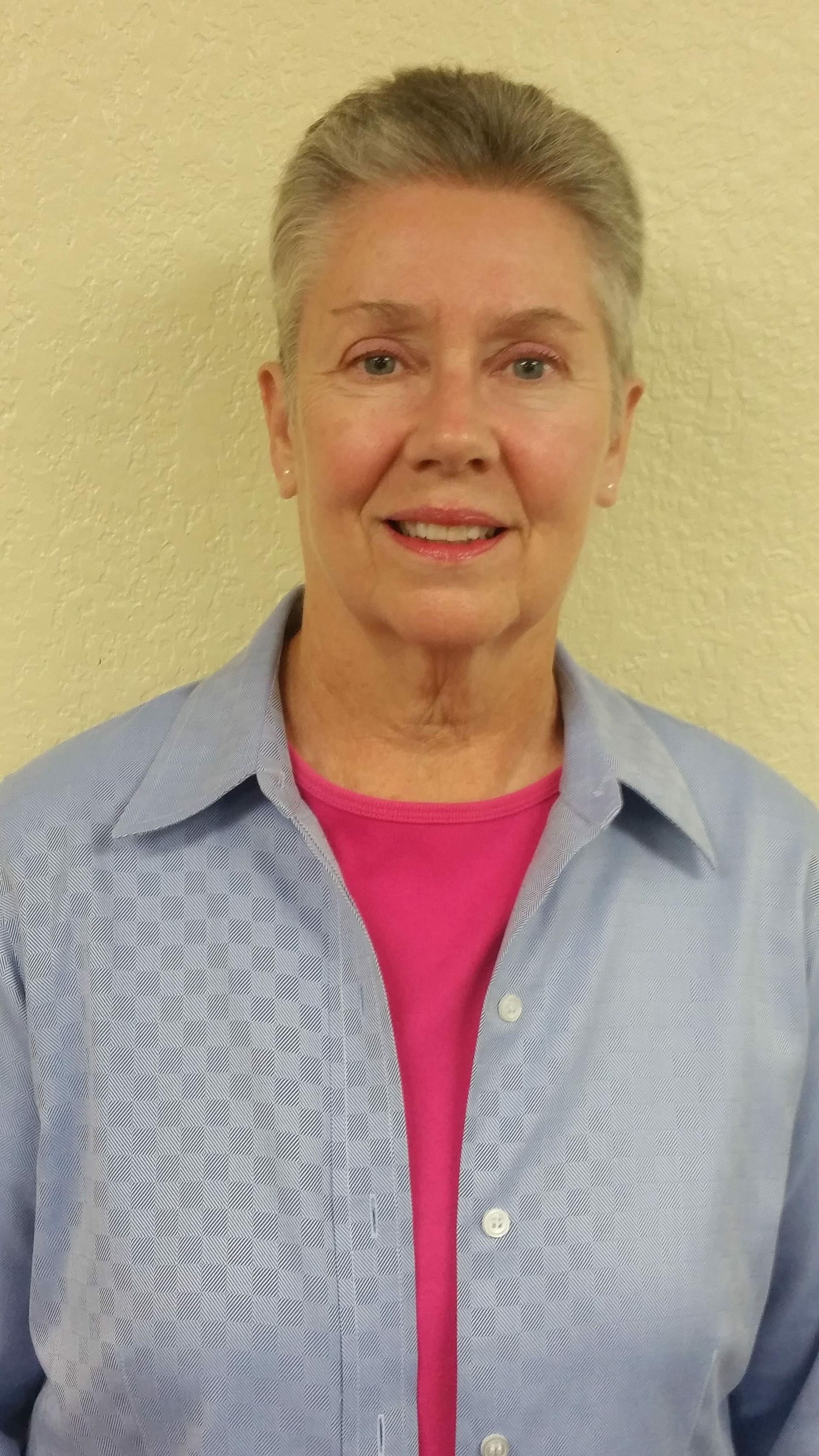 A woman wearing a blue shirt and a pink shirt is smiling for the camera.