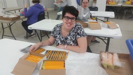 A woman is sitting at a table with boxes of pencils.