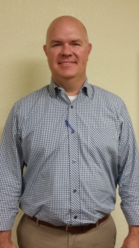 A bald man wearing a plaid shirt and khaki pants