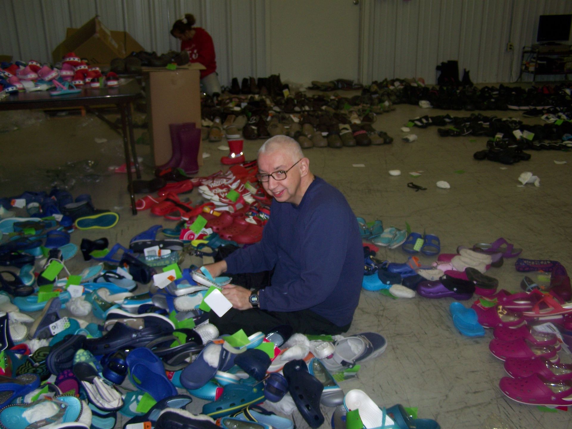 A man is sitting on the floor surrounded by shoes