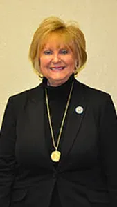 A woman in a black suit and gold necklace is smiling for the camera.