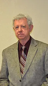 A man in a suit and tie is standing in front of a white wall.