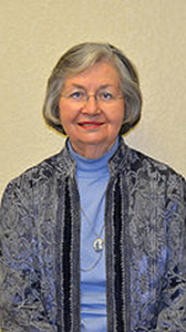 An older woman wearing glasses and a blue shirt is smiling for the camera.