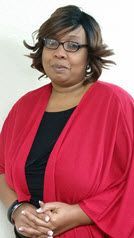 A woman wearing glasses and a red cardigan is standing in front of a white wall.