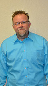 A man with a beard and glasses is wearing a blue shirt.