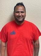 A man with a beard is wearing a red t-shirt and smiling.